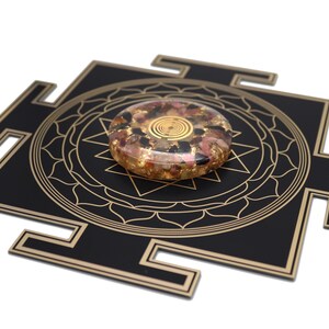 May include: A black and gold geometric design with a circular, multi-colored stone. The stone features gold flakes and a spiral design in the center. The design is on a white background.
