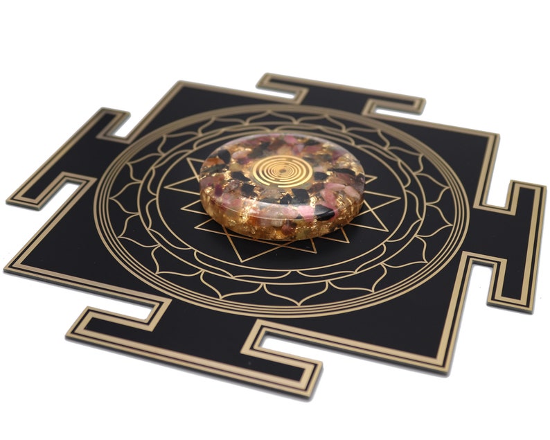 May include: A black and gold geometric design with a circular, multi-colored stone. The stone features gold flakes and a spiral design in the center. The design is on a white background.