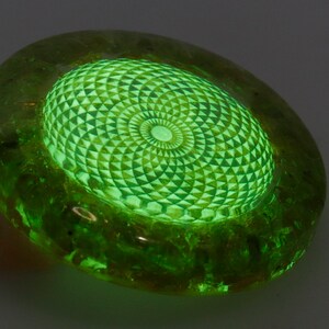 May include: A glowing green, oval-shaped decorative object. The center features a detailed geometric pattern in a lighter shade of green, radiating outwards. The outer edge of the object has a darker, textured appearance.