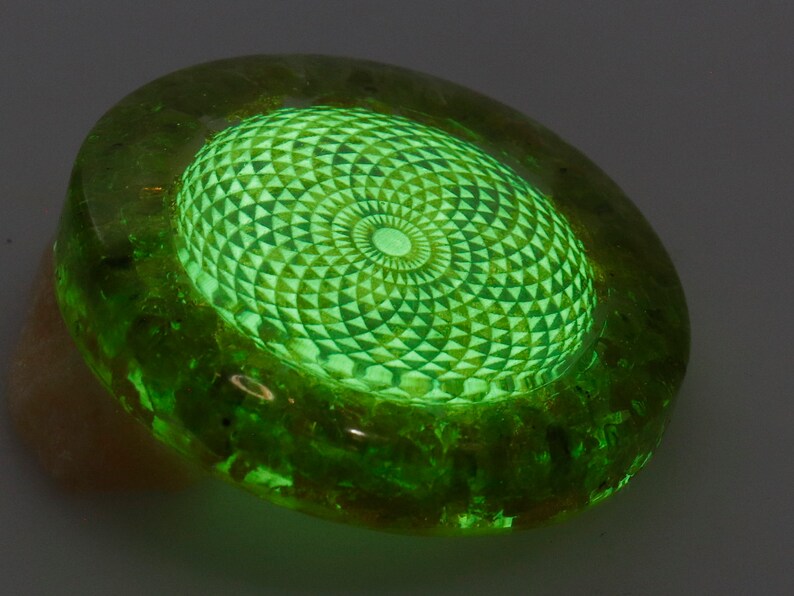 May include: A glowing green, oval-shaped decorative object. The center features a detailed geometric pattern in a lighter shade of green, radiating outwards. The outer edge of the object has a darker, textured appearance.