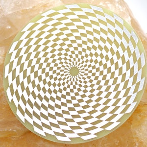 Può includere: Un disco circolare bianco e giallo con un motivo a spirale ipnotico di quadrati bianchi su uno sfondo giallo.