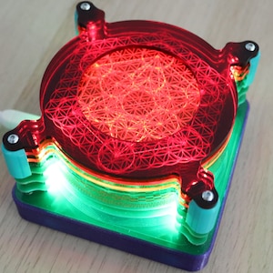 Könnte beinhalten: Eine mehrschichtige, kreisförmige Acrylskulptur in Rot-, Grün- und Blautönen. Die oberste Schicht zeigt ein rot lasergeschnittenes Design eines geometrischen Musters. Die Skulptur wird von innen beleuchtet und erzeugt so einen leuchtenden Effekt.