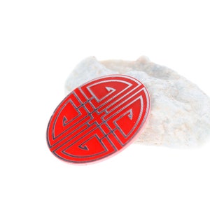 May include: A red and silver Chinese knot, also known as a lucky knot, on a white rock. The knot is a symbol of good fortune and prosperity.