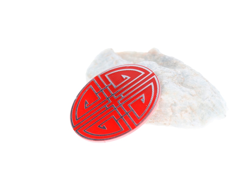 May include: A red and silver Chinese knot, also known as a lucky knot, on a white rock. The knot is a symbol of good fortune and prosperity.
