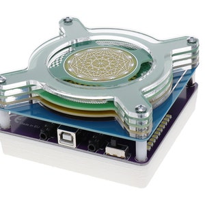 May include: A clear acrylic case with a circuit board and a green and white circular sensor inside. The case has a USB port and two audio jacks. The text "CE made in EU" is visible on the circuit board.