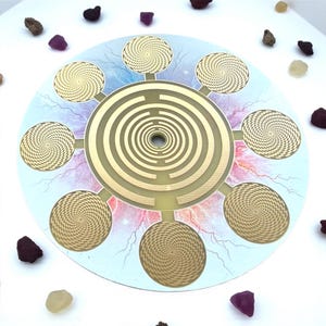 May include: A circular, gold-colored spiritual tool with a central labyrinth design and eight surrounding spiral patterns. The background features a blue and pink celestial design with scattered gemstones.