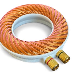 Könnte beinhalten: Eine kreisförmige Kupferspule mit weißer Basis und goldfarbenen Anschlüssen. Die Spule besteht aus eng gewickeltem Kupferdraht, der Orange- und Rosatöne aufweist. Die Anschlüsse haben rote und schwarze Akzente.