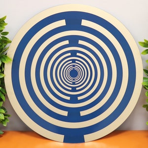 May include: A round, blue and cream colored decorative wall plate with concentric circles.