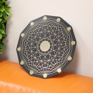 May include: A black octagonal plate with a gold geometric design and a spiral in the center. The plate has a raised edge and is decorated with gold dots around the perimeter.