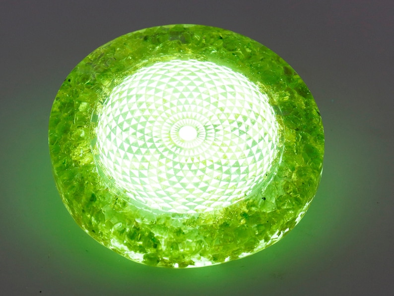 May include: A glowing, round, green decorative light fixture. The center features a geometric pattern, surrounded by a textured, green outer ring. The light emits a bright, white glow.