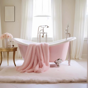 Op de afbeelding: Een roze bad met pootjes en een pluche roze deken eroverheen gelegd. Het bad staat in een badkamer met witte muren en witte gordijnen.