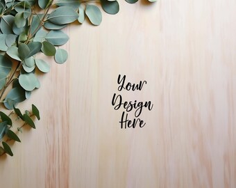 May include: A light wood background with a sprig of green eucalyptus leaves in the top left corner. The text "Your Design Here" is written in black cursive in the center of the image.