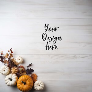 May include: White wood background with the text "Your Design Here" in black.  The bottom left corner of the image features a cluster of autumn-themed decorations, including white pumpkins, orange pumpkins, autumn leaves, and berries.