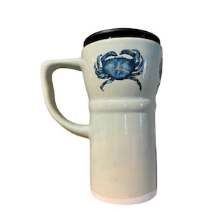 May include: A light green travel mug with a black lid and a white base. The mug features a blue crab illustration. The mug has a handle for easy carrying.