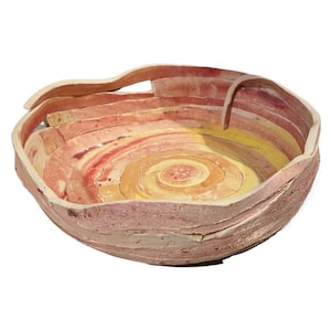 May include: A ceramic bowl with a spiral design in shades of yellow, orange, and red. The bowl is made of thin, layered strips of clay, giving it a unique and textured appearance.