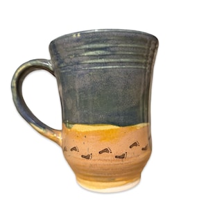 May include: A ceramic mug with a blue and yellow glaze. The mug has a handle and a design of footprints on the bottom.