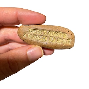 May include: A small, brown, speckled stone with the words "There's always a reason to smile" embossed in yellow.