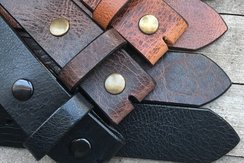 May include: Close-up of four leather belt straps with different colors and finishes. The straps have metal rivets and are arranged in a layered pattern.