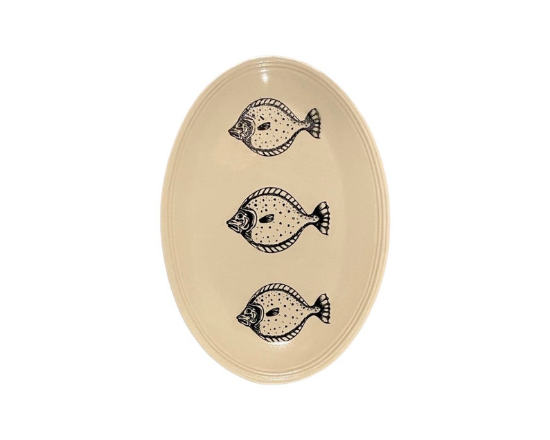 May include: A white oval ceramic serving platter with a black and white fish design. The platter features three fish, each with a unique pattern and a slightly different pose.
