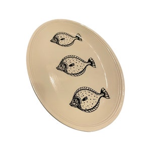 May include: A white oval serving platter with a black outline of three fish. The fish are facing the same direction and have a dotted pattern.