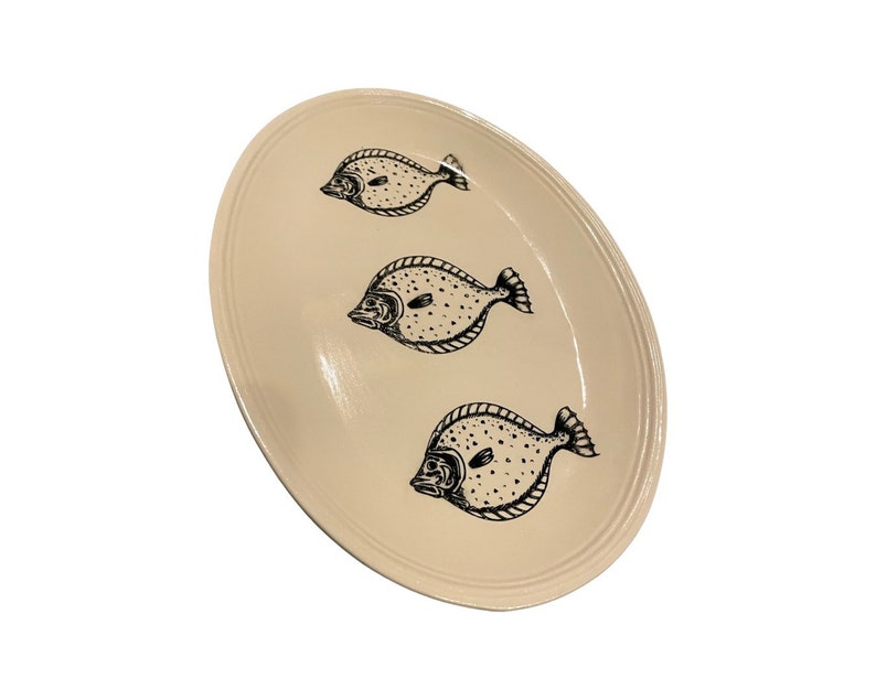 May include: A white oval serving platter with a black outline of three fish. The fish are facing the same direction and have a dotted pattern.
