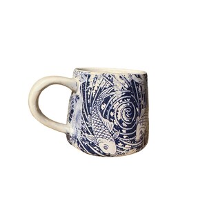 May include: A ceramic mug with a white handle and a blue and white koi fish design. The mug has a textured surface and a curved handle. The design includes koi fish and swirling water patterns. Ideal for tea or coffee.