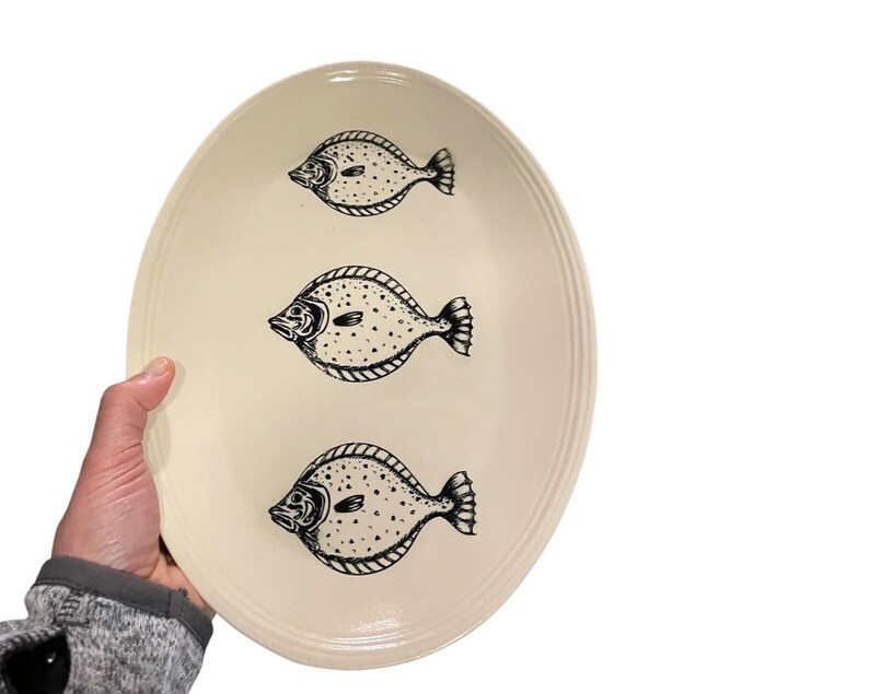 May include: A white oval ceramic serving platter with three black and white fish illustrations.
