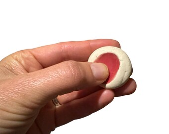 May include: A round, white cookie with a red center. The cookie is slightly flattened and has a rough texture.