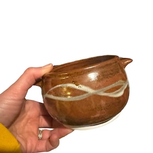 May include: A small brown ceramic bowl with white glaze accents. The bowl has a rounded shape and a slightly flared rim.