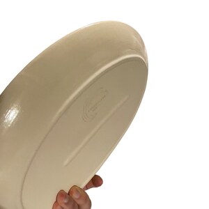 May include: A large, off-white ceramic serving dish with a slightly rounded shape. The dish has a smooth, glossy finish and a subtle lip around the edge.