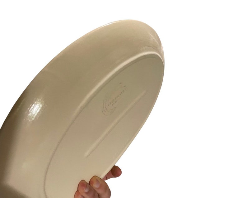 May include: A large, off-white ceramic serving dish with a slightly rounded shape. The dish has a smooth, glossy finish and a subtle lip around the edge.