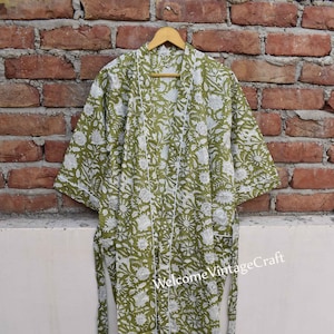 May include: A green cotton robe with a white floral print and a white trim. The robe has a tie belt and is hanging on a wooden hanger.