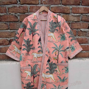 May include: A pink quilted robe with a tropical print featuring palm trees, leopards, and toucans. The robe has a striped trim and two pockets.