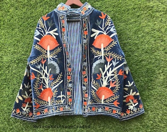 May include: A blue velvet jacket featuring intricate floral embroidery in shades of orange, white, and grey. The garment has a high collar, long sleeves, and an open front design that reveals a blue and white striped lining on the interior.