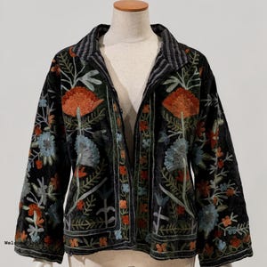 May include: A black jacket featuring long sleeves and a collared neckline, adorned with intricate floral embroidery in shades of orange, light blue, and green. The garment has a button-front closure and a black and white striped inner collar lining.