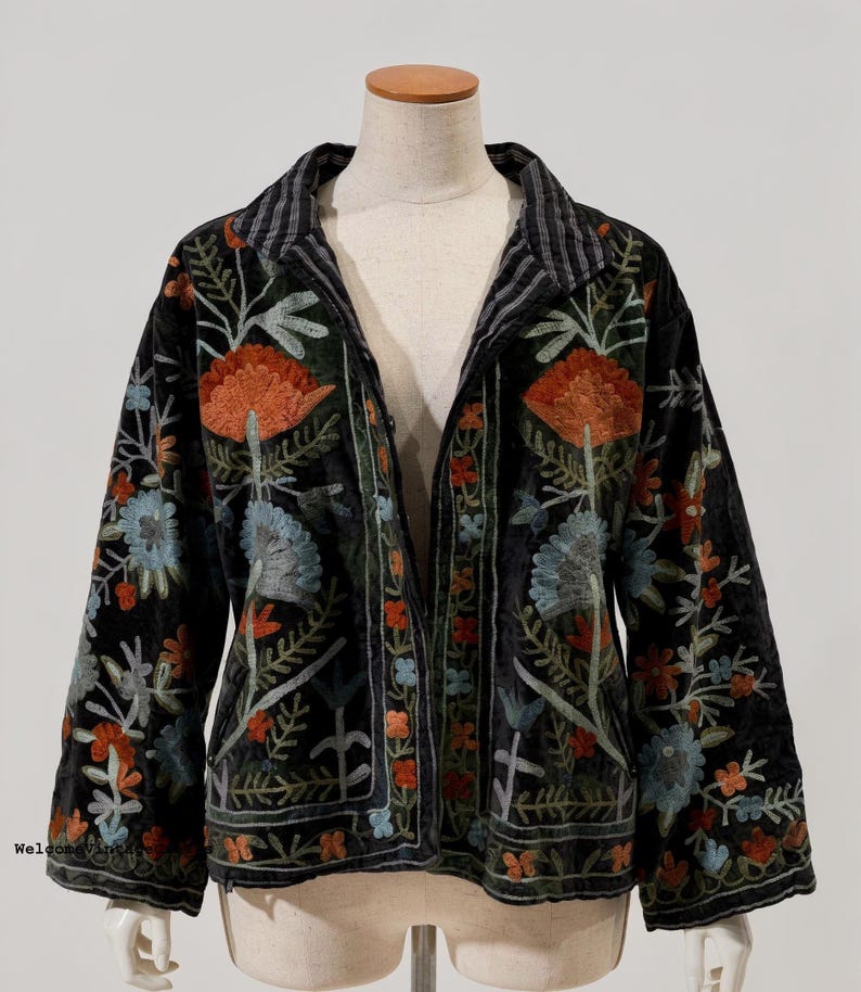 May include: A black jacket featuring long sleeves and a collared neckline, adorned with intricate floral embroidery in shades of orange, light blue, and green. The garment has a button-front closure and a black and white striped inner collar lining.