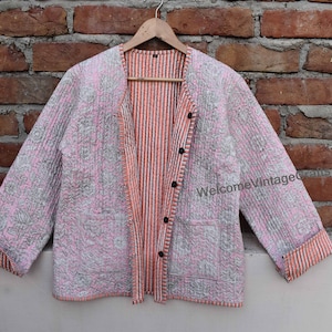 Puede incluir: Una chaqueta acolchada reversible con un estampado floral rosa en un lado y un patrón a rayas en el otro. La chaqueta tiene un cierre de botón y un bolsillo en la parte delantera.