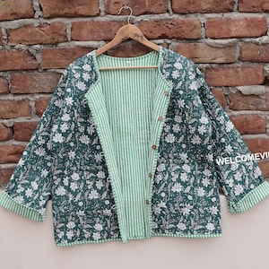 Può includere: Una giacca trapuntata con motivo floreale verde e bianco con fodera a righe. La giacca ha una chiusura con bottoni e un colletto.