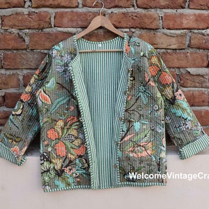 Puede incluir: Una chaqueta acolchada verde y gris con estampado floral. La chaqueta tiene un forro a rayas y un diseño sin cuello.