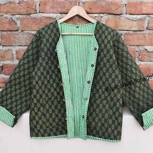 Könnte beinhalten: Eine reversible gesteppte Jacke mit einem grün-weiß gestreiften Futter. Eine Seite der Jacke ist dunkelgrün mit einem kleinen Blumenmuster, die andere Seite ist einfarbig dunkelgrün. Die Jacke hat einen Knopfverschluss und lange Ärmel.
