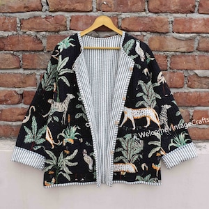 Puede incluir: Una chaqueta acolchada negra con un diseño reversible. Un lado presenta un fondo negro con un estampado tropical blanco y verde con animales. El otro lado es un patrón de rayas blancas y negras. La chaqueta tiene un cierre de botón y mangas largas.