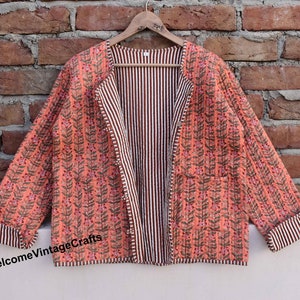 Pode incluir: Uma jaqueta acolchoada reversível com estampa floral de um lado e padrão listrado do outro. A jaqueta tem uma bainha listrada marrom e branca e um bolso no lado floral.