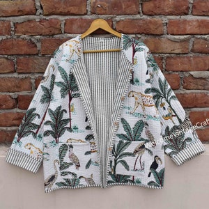 Puede incluir: Una chaqueta acolchada blanca con un forro a rayas blanco y negro. La chaqueta presenta un estampado tropical con palmeras, leopardos y pájaros. El texto "Welcome VintageCrafts" es visible en la manga derecha.