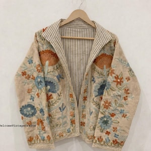 May include: A beige jacket featuring intricate floral embroidery in shades of orange, blue, and green. The garment has a notched collar and an interior lining with a black and white vertical pinstripe pattern. The text WelcomeVintageCrafts is visible.
