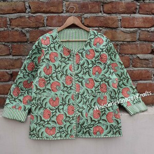 May include: A green quilted jacket with a floral print featuring pink flowers and green leaves. The jacket has a white and green striped trim around the edges and pockets.