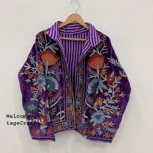 May include: A purple velvet jacket featuring intricate floral embroidery in shades of orange, blue, and white. The jacket has a collared neckline, long sleeves, and an interior lining with a purple and white vertical stripe pattern.