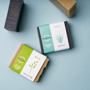 May include: Three bars of soap with green and white labels. The labels say "your body our planet facial bar" and have different ingredients listed. The labels also say "Oetee" and have a detox or healing theme.