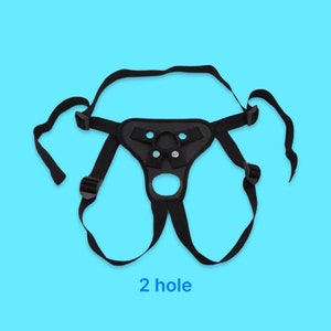 May include: Black leather harness with two adjustable straps and a metal ring. The harness has a large oval opening in the front and two smaller holes on the sides. The text "2 hole" is printed below the harness.