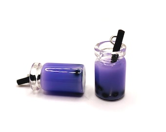May include: A pair of purple bubble tea charm earrings with a black straw. The earrings are made of resin and are shaped like a glass of bubble tea.