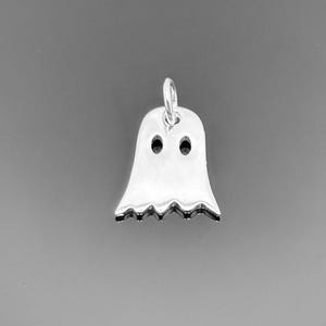 May include: A silver ghost charm with two eye holes and a scalloped lower edge. The charm has a small loop at the top for attaching to a necklace or bracelet. The ghost is a classic Halloween or spooky-themed design.